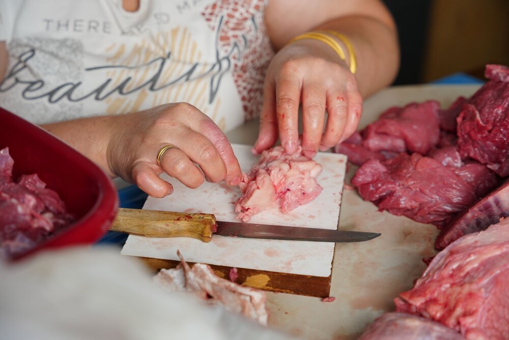 Hands trimming fat from beef pieces on a cutting board before packing