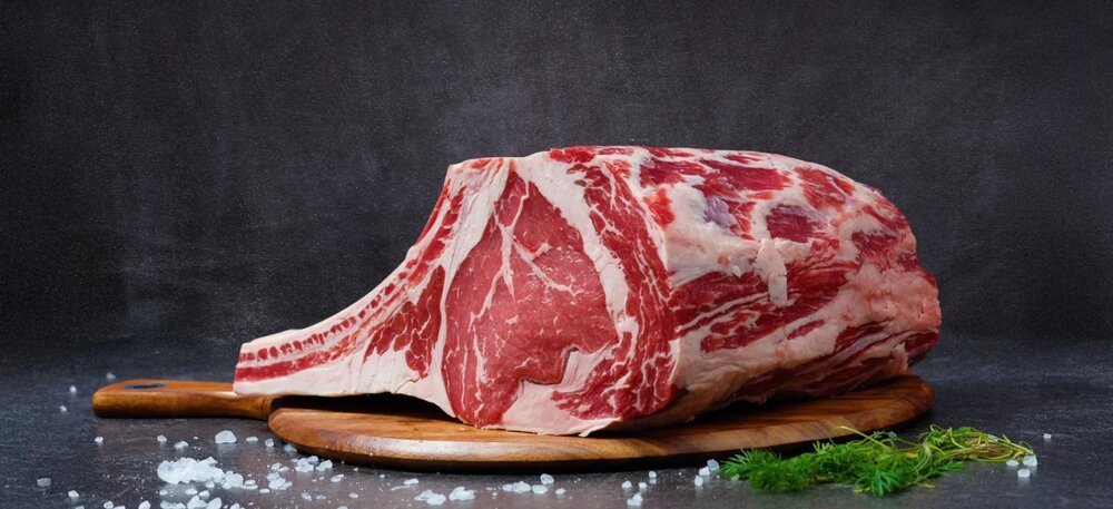 A whole bone-in beef rib on a wooden board before cutting and packing