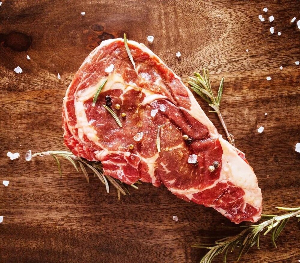 A raw beef ribeye steak with rosemary and coarse salt on a wooden board